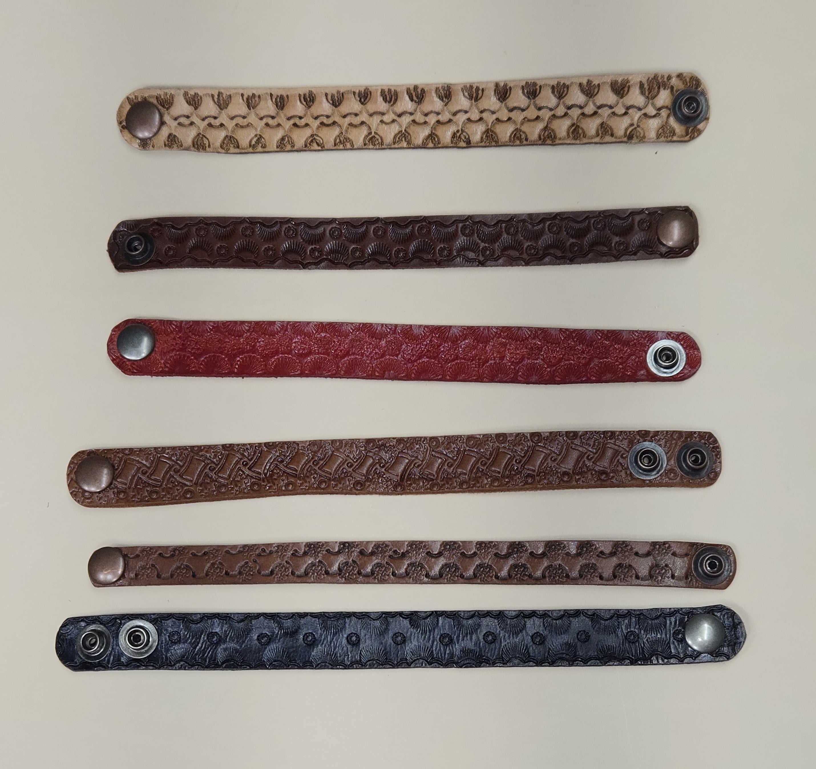 Five leather bracelets with embossed patterns on a light beige background